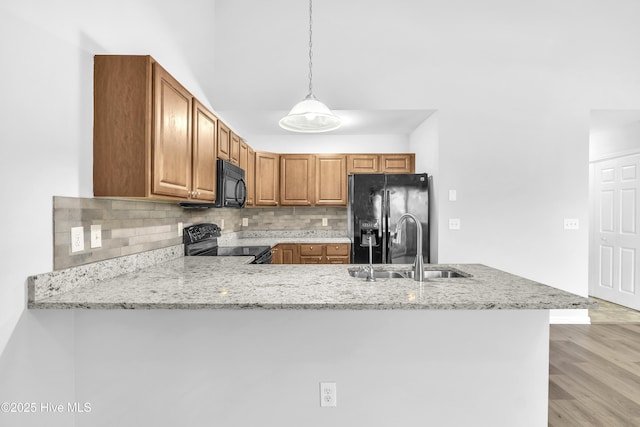 kitchen with decorative light fixtures, black appliances, sink, light stone counters, and kitchen peninsula