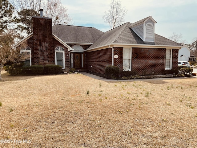 view of front of home with brick siding, a chimney, a front yard, and roof with shingles