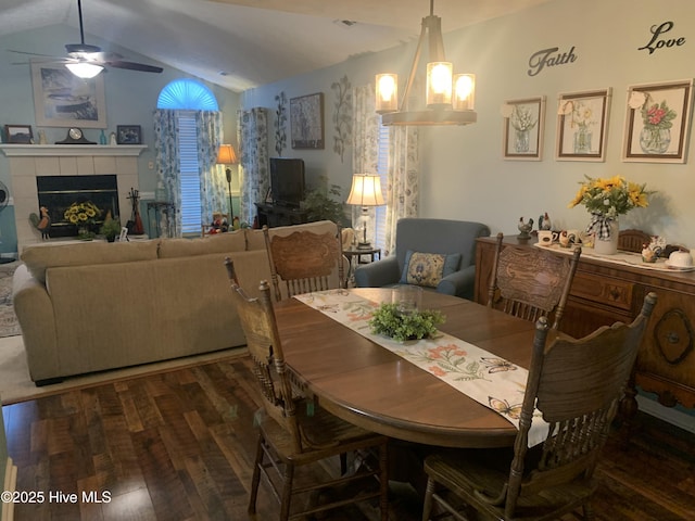 dining room with a tiled fireplace, lofted ceiling, dark hardwood / wood-style floors, and ceiling fan with notable chandelier