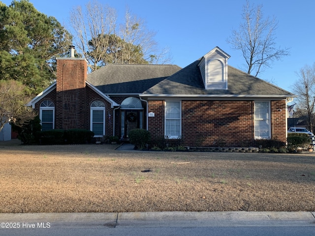 view of front of house featuring brick siding, a chimney, and a front lawn