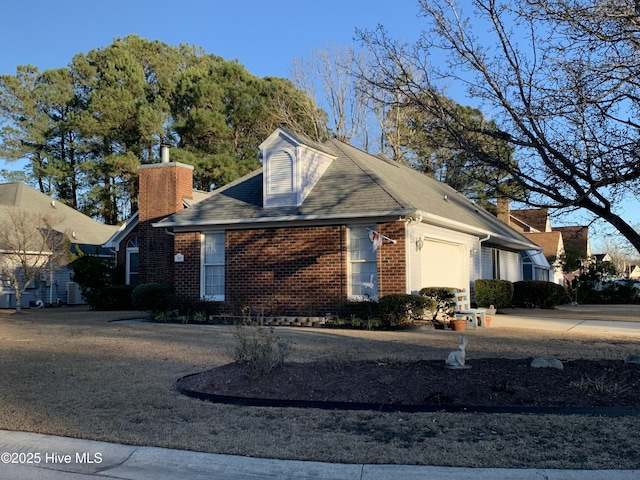 view of front of home with brick siding, an attached garage, a chimney, and driveway