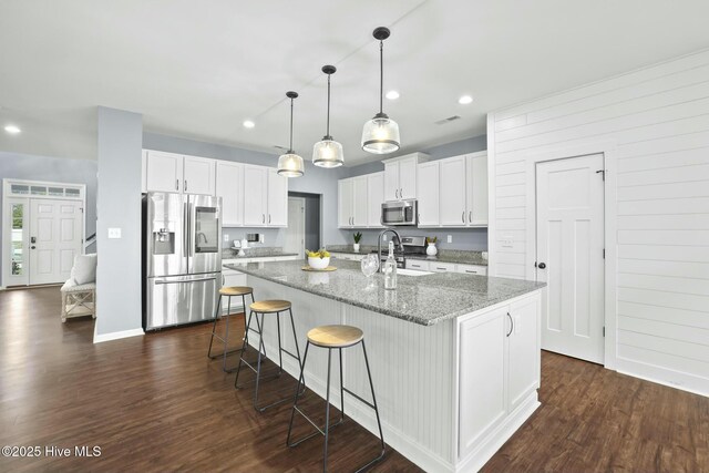 kitchen featuring stone counters, stainless steel appliances, an island with sink, and white cabinets