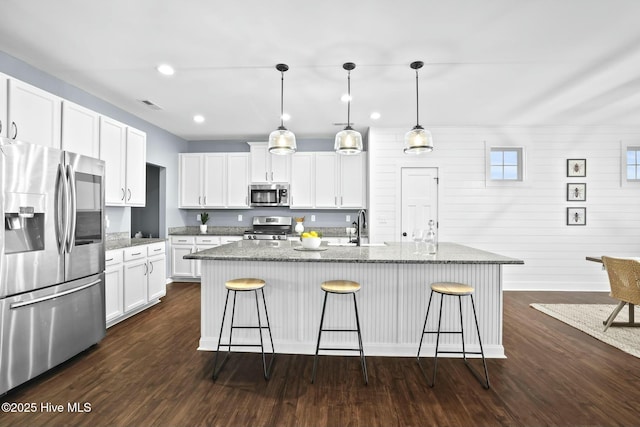 kitchen featuring pendant lighting, white cabinetry, stainless steel appliances, light stone countertops, and a center island with sink