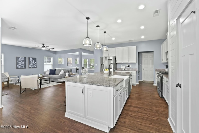 kitchen with pendant lighting, white cabinets, a kitchen island with sink, stainless steel appliances, and dark wood-type flooring