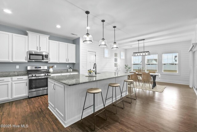 kitchen featuring a breakfast bar area, white cabinetry, hanging light fixtures, stainless steel appliances, and a kitchen island with sink