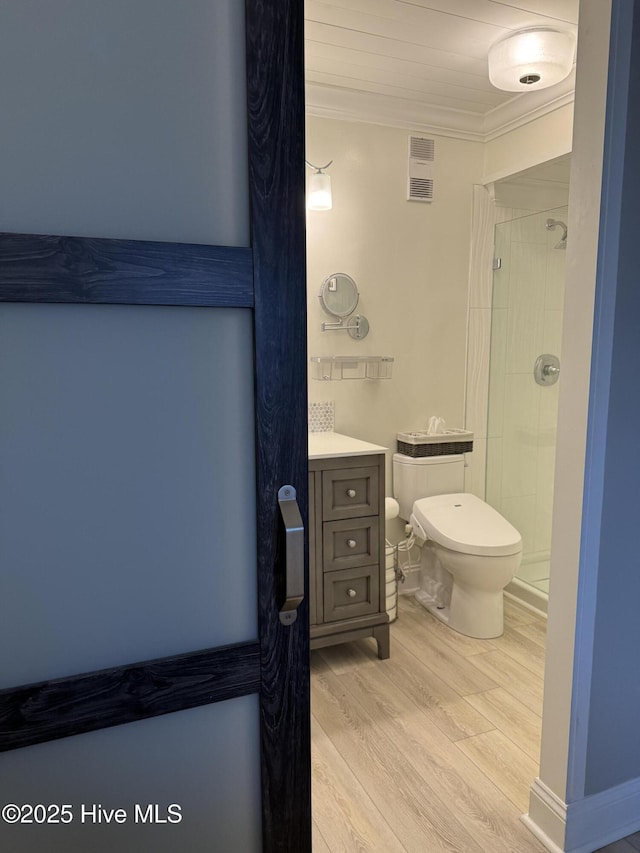 bathroom featuring hardwood / wood-style flooring, ornamental molding, vanity, tiled shower, and toilet