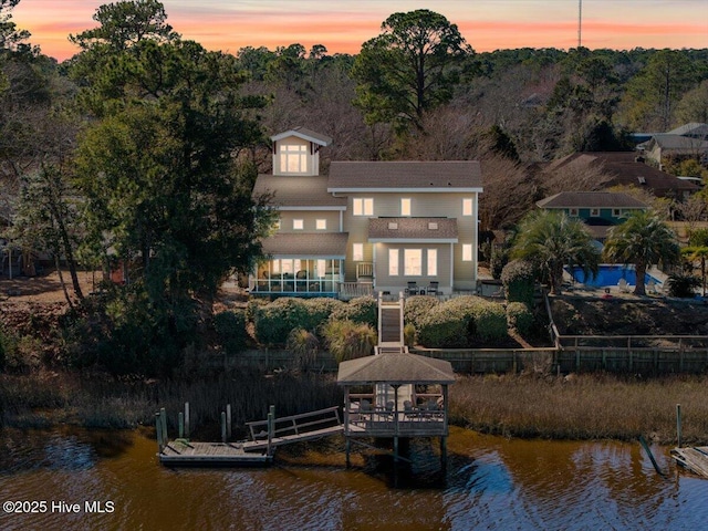 back of house at dusk featuring a balcony, a gazebo, a water view, and fence