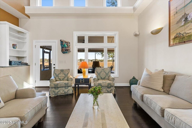living area with dark wood-type flooring, a towering ceiling, and baseboards