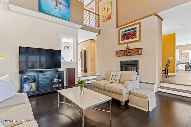 living area featuring an inviting chandelier, a towering ceiling, dark wood-style floors, and a glass covered fireplace