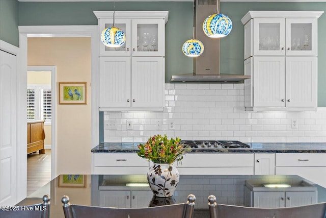 kitchen featuring stainless steel gas cooktop, wall chimney range hood, backsplash, and white cabinets