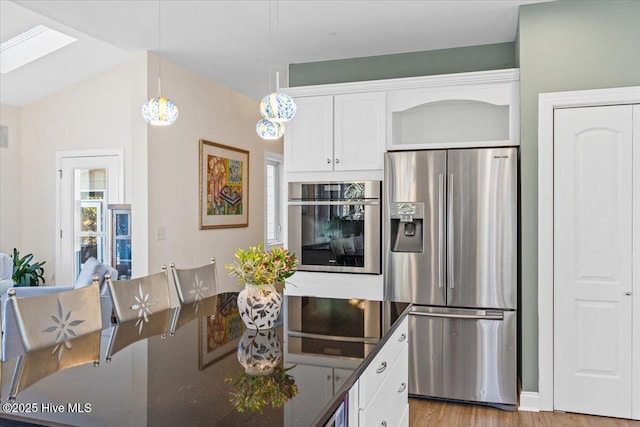 kitchen with stainless steel appliances, a skylight, white cabinetry, light wood finished floors, and decorative light fixtures