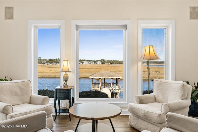 sitting room featuring plenty of natural light, a water view, wood finished floors, and visible vents