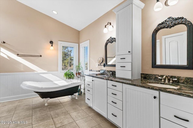 full bath featuring a wainscoted wall, a sink, double vanity, and lofted ceiling