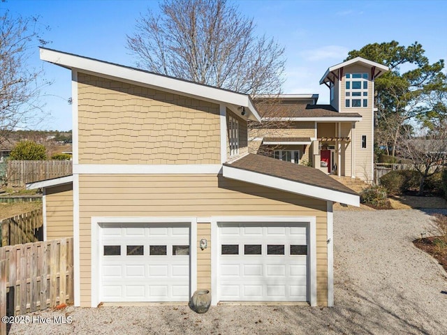 view of front facade featuring a garage, fence, and gravel driveway