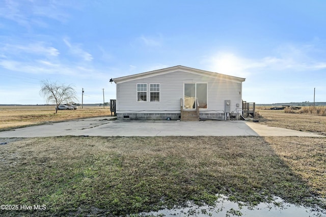 back of house with a rural view, a patio, and a lawn