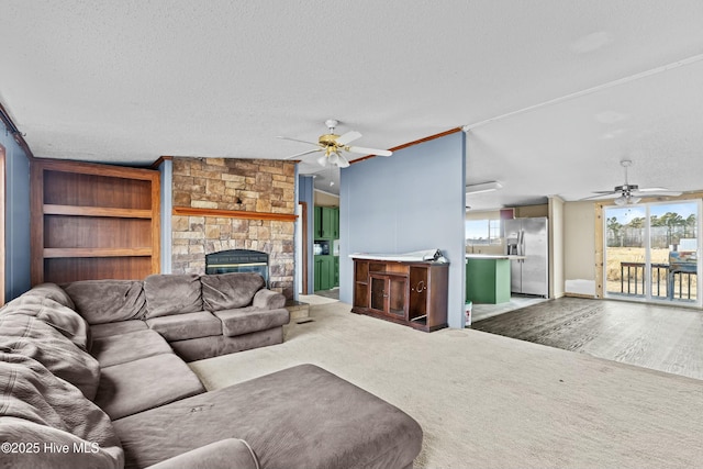 living room featuring ceiling fan, carpet flooring, a stone fireplace, and a textured ceiling