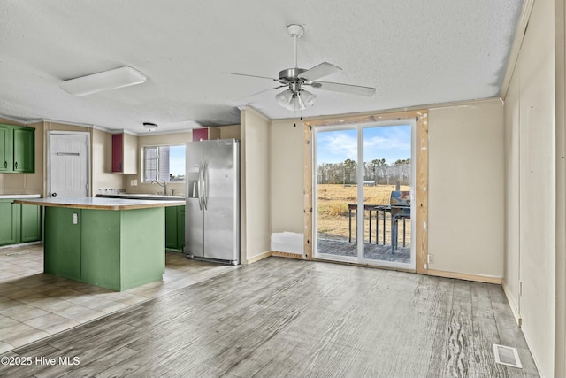 kitchen with a wealth of natural light, a kitchen island, green cabinets, and stainless steel fridge