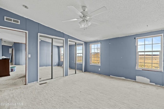 unfurnished bedroom featuring multiple closets, vaulted ceiling, carpet, and a textured ceiling