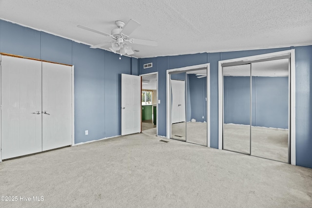 unfurnished bedroom with multiple closets, light colored carpet, ceiling fan, and a textured ceiling