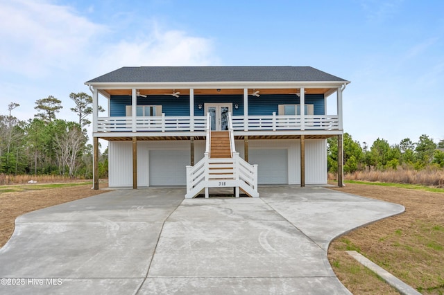 coastal inspired home with an attached garage, a shingled roof, stairway, and concrete driveway