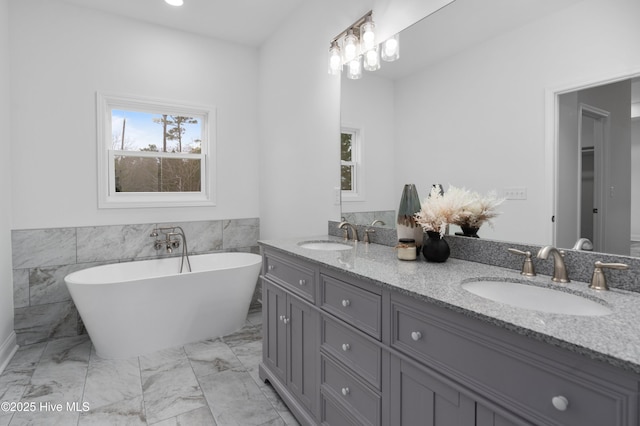 bathroom with double vanity, marble finish floor, a freestanding bath, and a sink