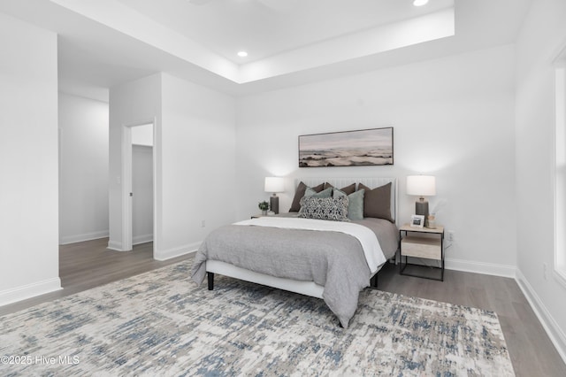 bedroom featuring a tray ceiling, recessed lighting, wood finished floors, and baseboards