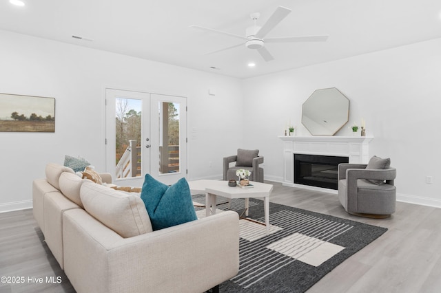 living area with french doors, recessed lighting, light wood-style floors, a glass covered fireplace, and baseboards