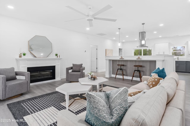 living room with light wood-style floors, recessed lighting, a glass covered fireplace, and a ceiling fan