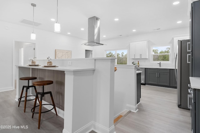 kitchen with white cabinets, a kitchen island, a kitchen breakfast bar, island exhaust hood, and light countertops