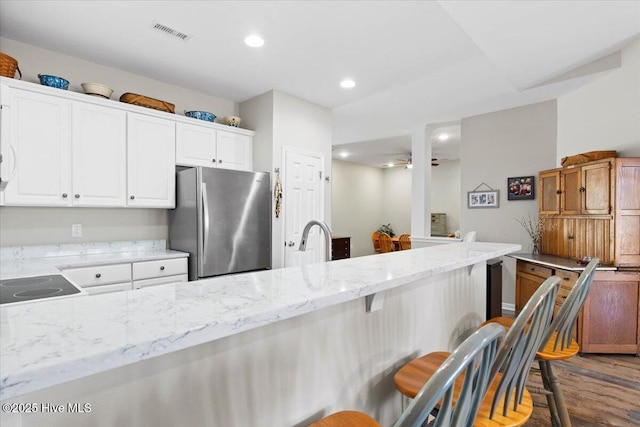 kitchen featuring a kitchen breakfast bar, white cabinetry, light stone countertops, and stainless steel refrigerator