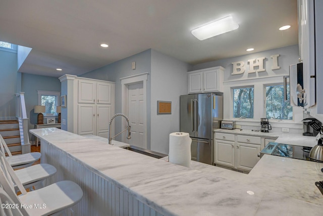 kitchen with white cabinetry, a kitchen bar, stainless steel fridge, and plenty of natural light