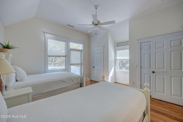 bedroom featuring lofted ceiling, ceiling fan, multiple closets, and light wood-type flooring