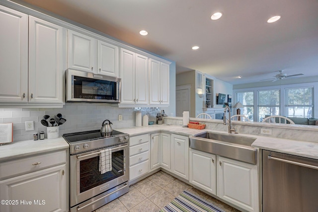 kitchen with light tile patterned flooring, appliances with stainless steel finishes, tasteful backsplash, white cabinetry, and sink