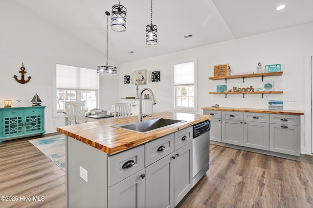 kitchen featuring sink, wooden counters, decorative light fixtures, a center island with sink, and dishwasher