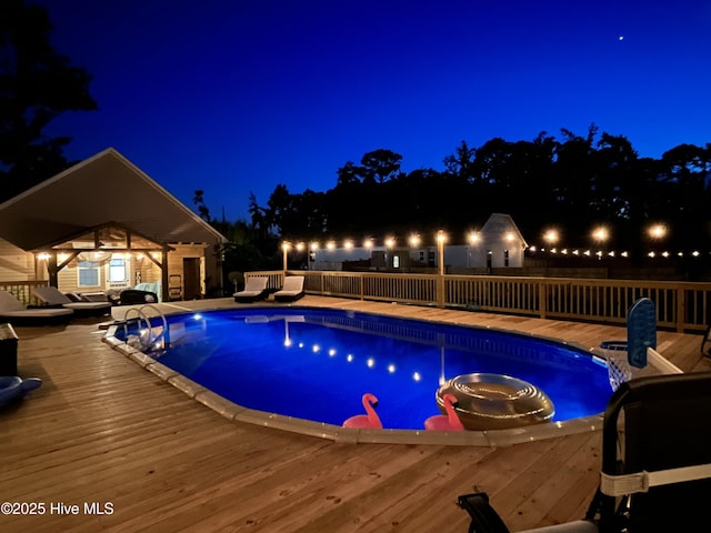 pool at night featuring a wooden deck and an outdoor structure