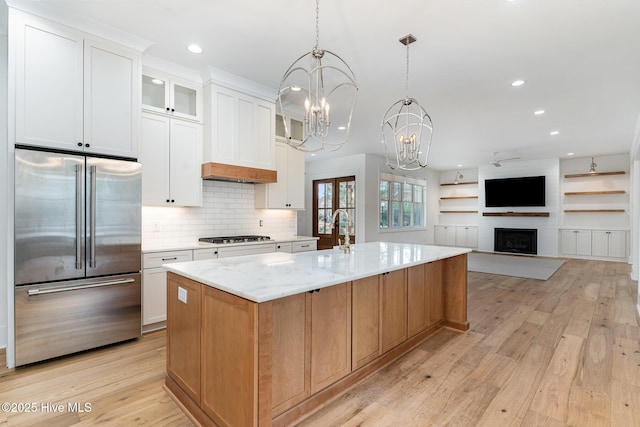 kitchen featuring light stone counters, hanging light fixtures, appliances with stainless steel finishes, a kitchen island with sink, and white cabinets