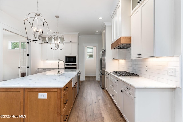 kitchen with light stone counters, hanging light fixtures, a center island with sink, appliances with stainless steel finishes, and white cabinets