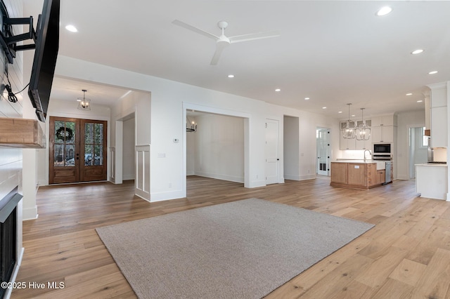 unfurnished living room featuring sink, ceiling fan with notable chandelier, and light wood-type flooring