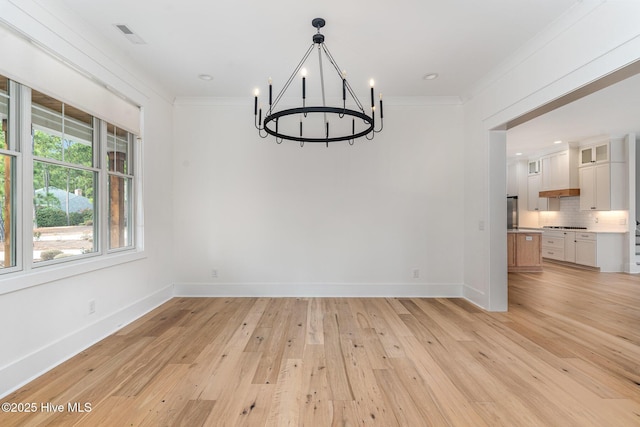 unfurnished dining area with an inviting chandelier, crown molding, and light wood-type flooring