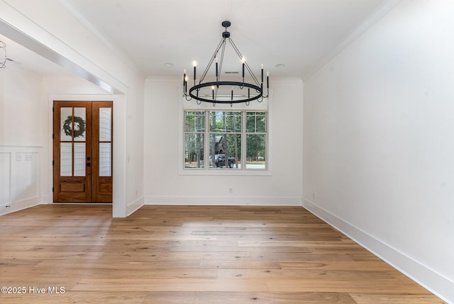 unfurnished dining area with french doors, crown molding, a notable chandelier, and light hardwood / wood-style flooring