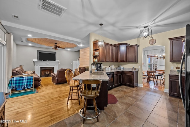 kitchen featuring dark brown cabinetry, sink, a breakfast bar area, decorative light fixtures, and light stone countertops