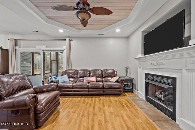 living room featuring wood ceiling, ornamental molding, a raised ceiling, and light wood-type flooring