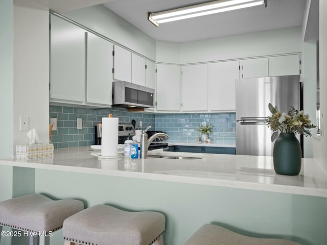 kitchen featuring appliances with stainless steel finishes, a breakfast bar area, decorative backsplash, and white cabinets