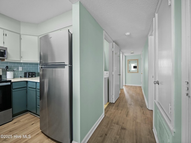 kitchen with light hardwood / wood-style flooring, appliances with stainless steel finishes, white cabinetry, tasteful backsplash, and a textured ceiling