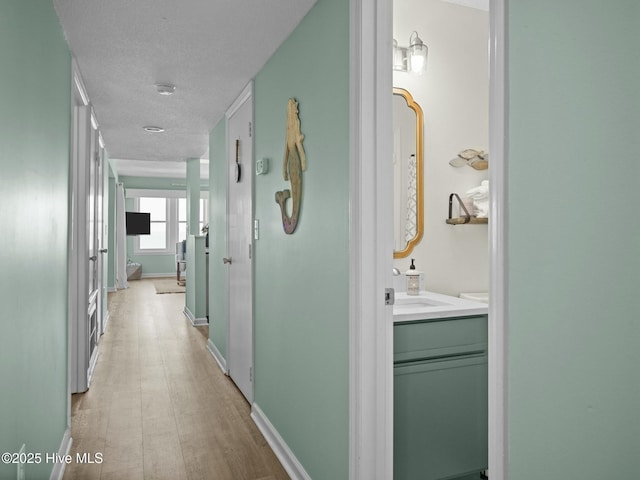 corridor featuring sink, a textured ceiling, and light wood-type flooring