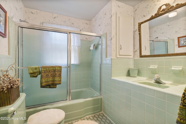 full bathroom with tile walls, sink, bath / shower combo with glass door, and toilet