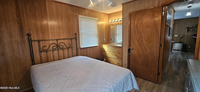 bedroom featuring dark hardwood / wood-style flooring, wooden walls, ornamental molding, and ceiling fan