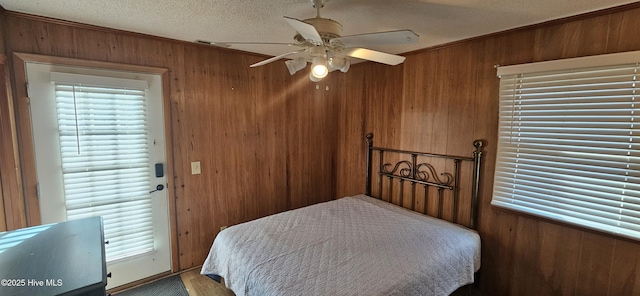 bedroom featuring ceiling fan, wooden walls, ornamental molding, and a textured ceiling