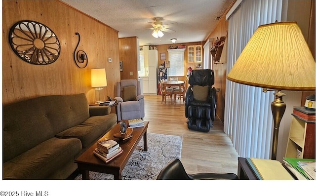 living room with a textured ceiling, ornamental molding, wooden walls, ceiling fan, and light hardwood / wood-style floors