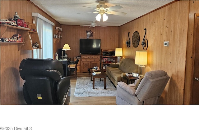 living room with light hardwood / wood-style flooring, ceiling fan, wooden walls, ornamental molding, and a textured ceiling